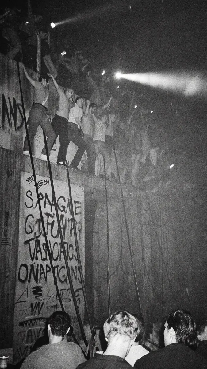 Archival night photograph of crowds climbing the Berlin Wall.